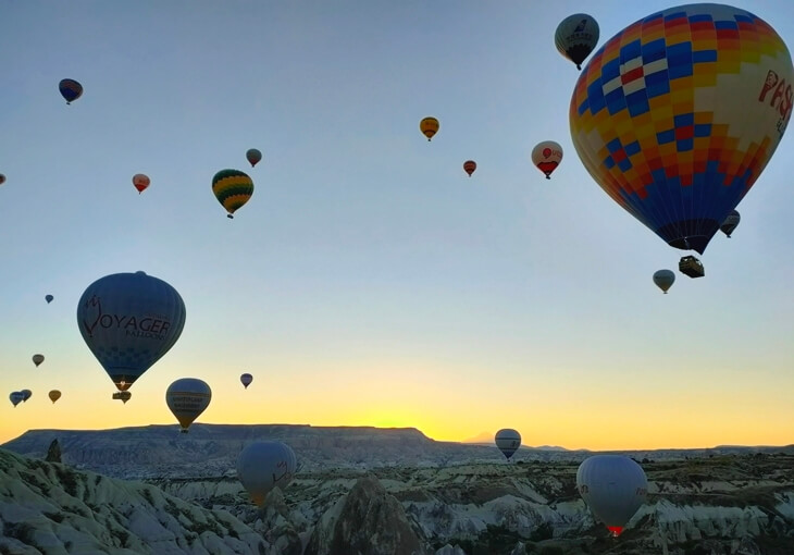Gün doğumunda Kapadokya Aşk Vadisi üzerinde uçan sıcak hava balonları ve vadinin kaya dokusu